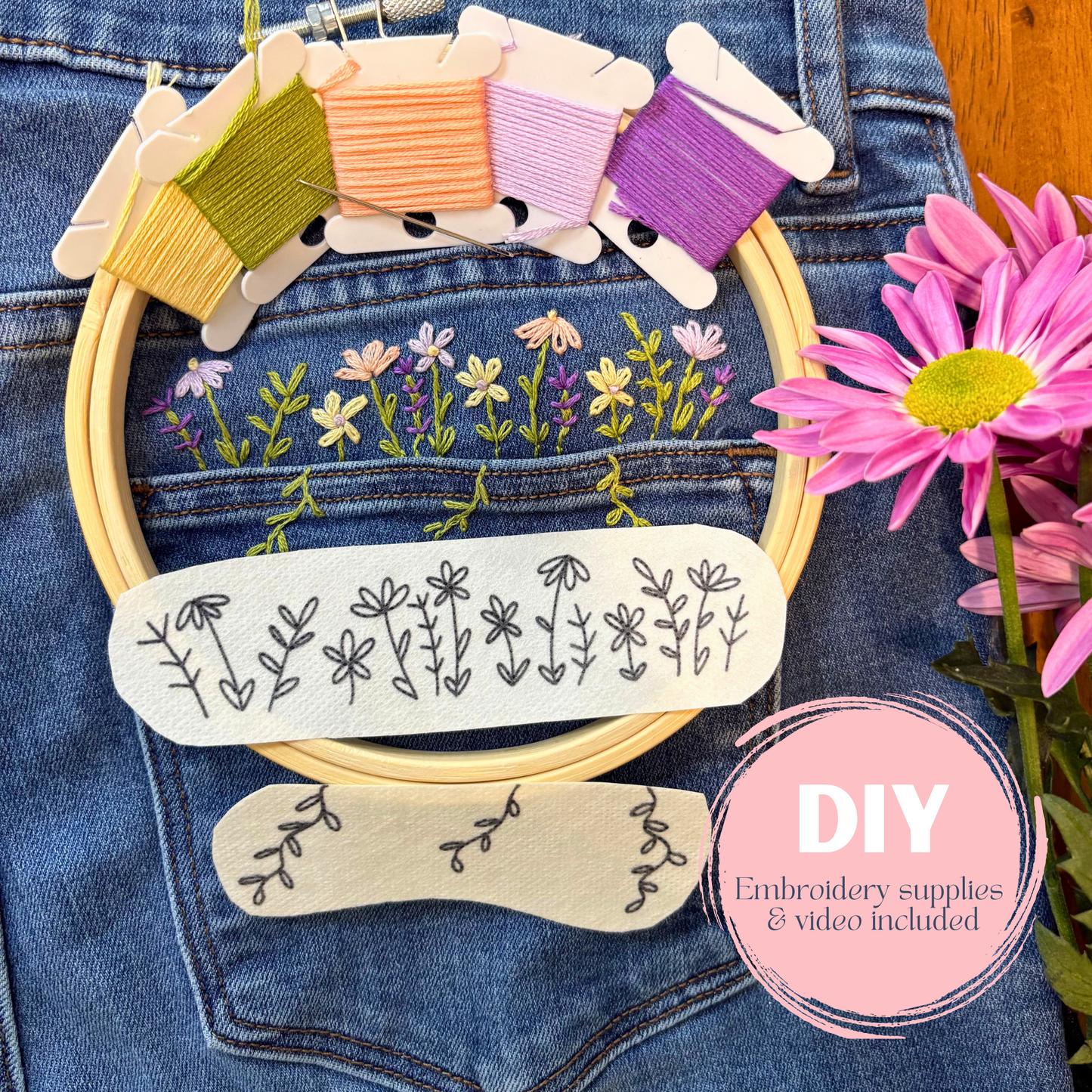 Embroidery hoop with floral patterns and embroidery threads on denim fabric, surrounded by flowers.