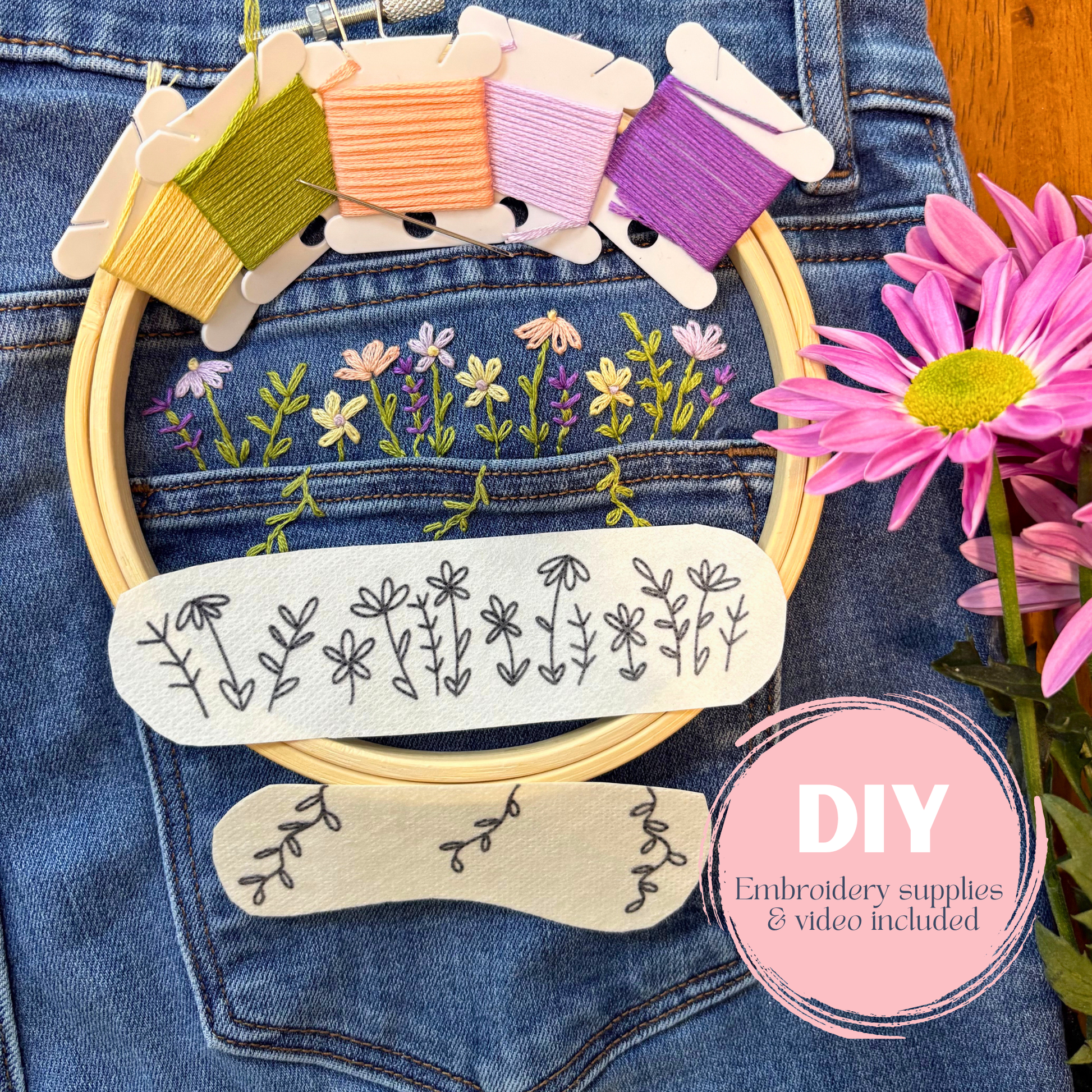 Embroidery hoop with floral patterns and embroidery threads on denim fabric, surrounded by flowers.