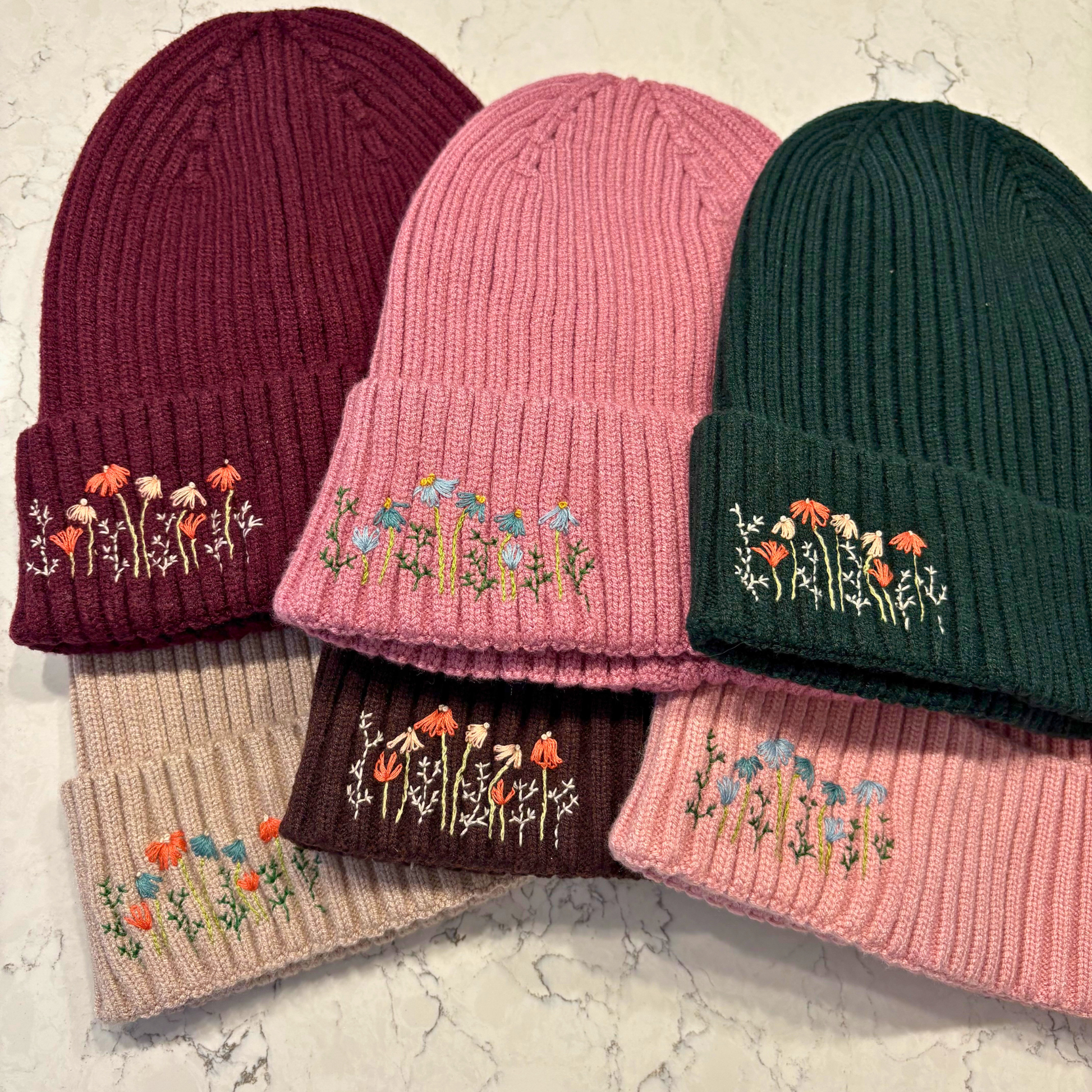 6 beanies with dainty embroidered floral design in bottom left corner.