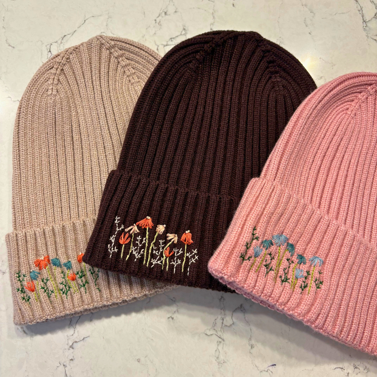 3 beanies with dainty embroidered floral design in bottom left corner.