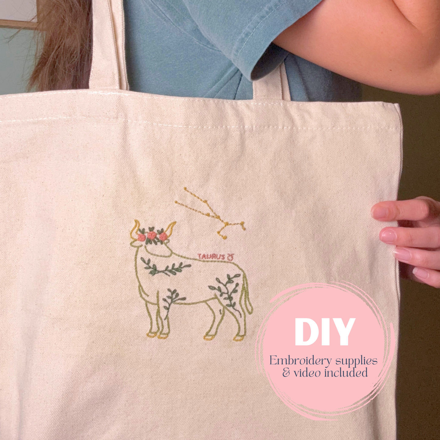 Person holding a tote bag with embroidered design of Taurus zodiac sign, DIY text overlay.