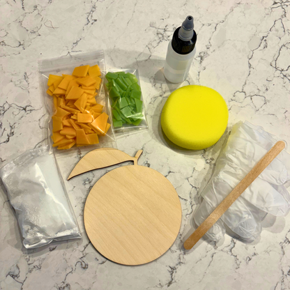 Kit items including a glue bottle, yellow sponge, stained glass, and wooden coasters on a marble surface.