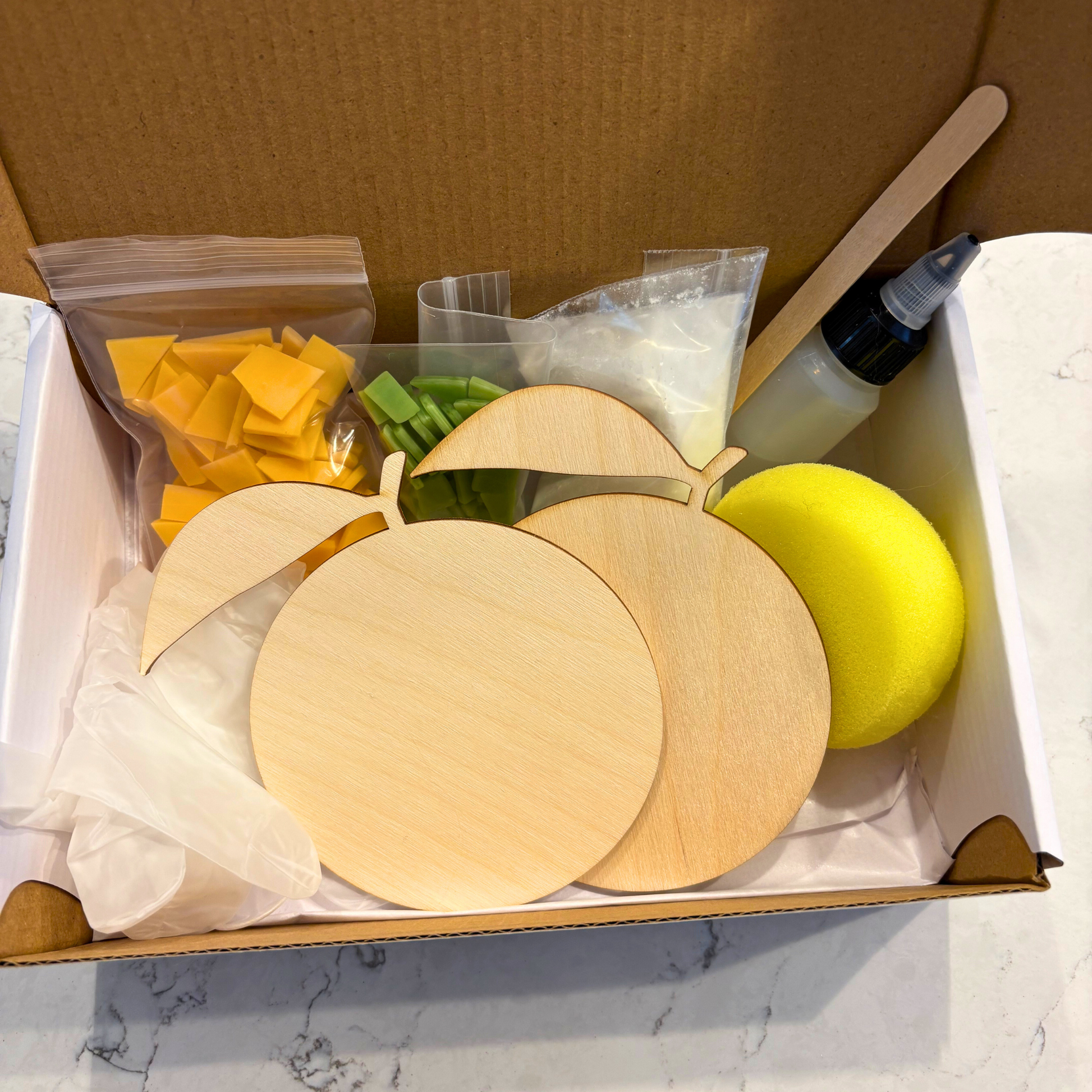 Crafting kit with wooden oranges, green stained glass, foam sponge, and other supplies in a box.