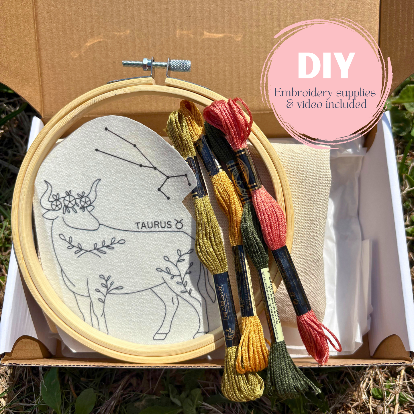 Embroidery hoop with Taurus constellation design and colorful threads, set against a natural background.