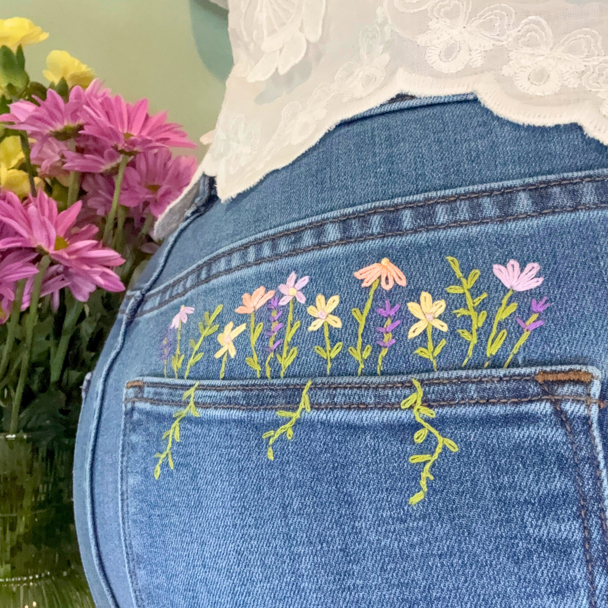 Blue denim jacket with floral embroidery on a blurred background of flowers
