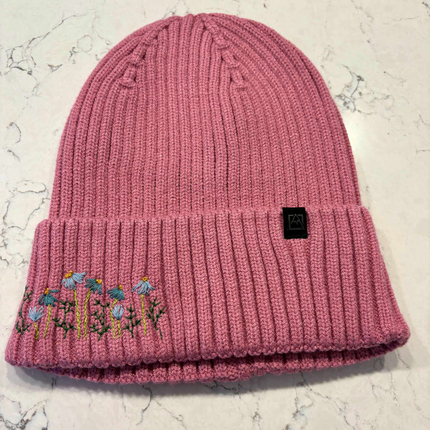 Mauve beanie with dainty embroidered floral design in bottom left corner.