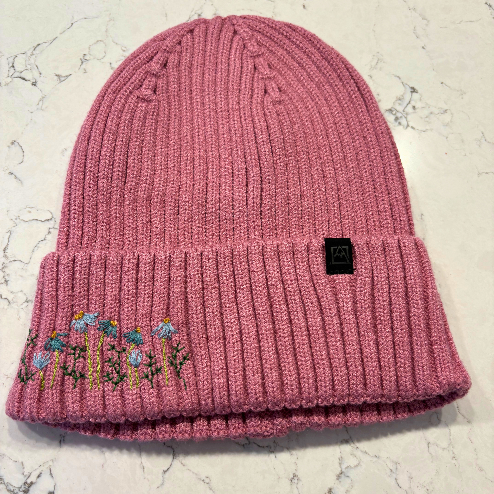 Mauve beanie with dainty embroidered floral design in bottom left corner.