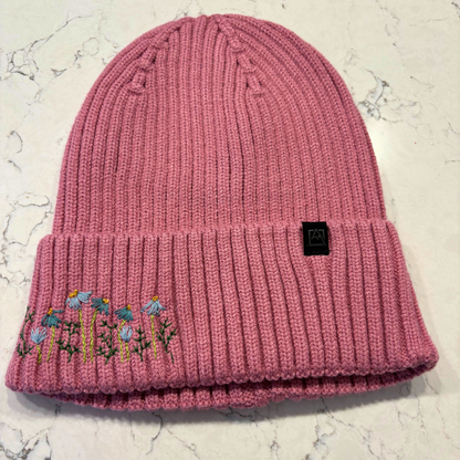 Mauve beanie with dainty embroidered floral design in bottom left corner.