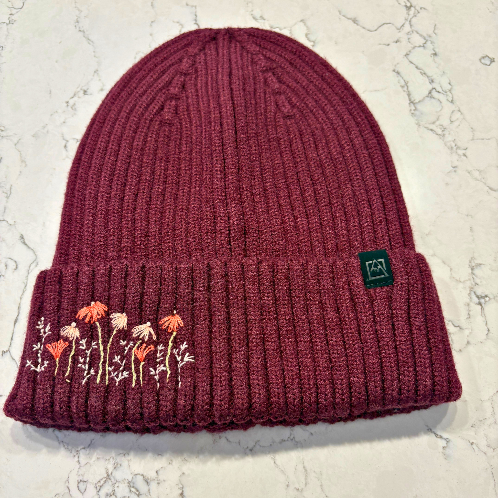 Maroon beanie with dainty embroidered floral design in bottom left corner.