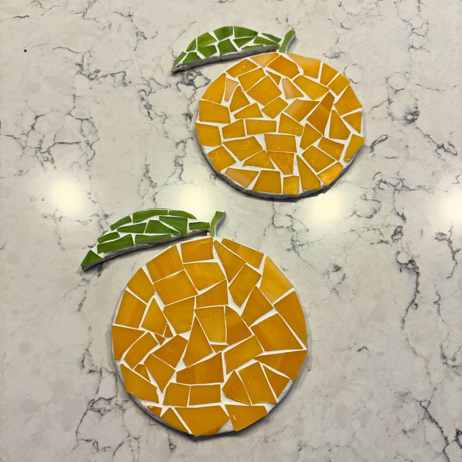 Two mosaic orange coasters on a marble surface