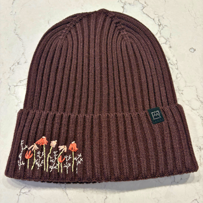 Brown beanie with dainty embroidered floral design in bottom left corner.