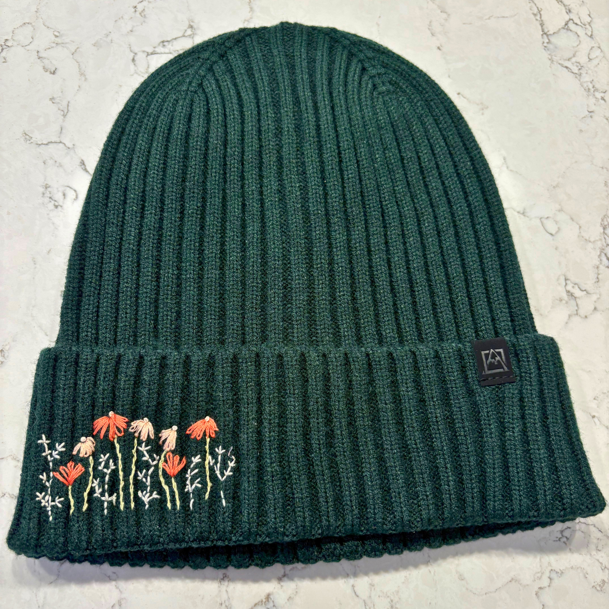 Forest green beanie with dainty embroidered floral design in bottom left corner.