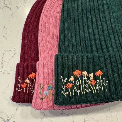 Three knitted hats in different colors with floral embroidery on a marble background
