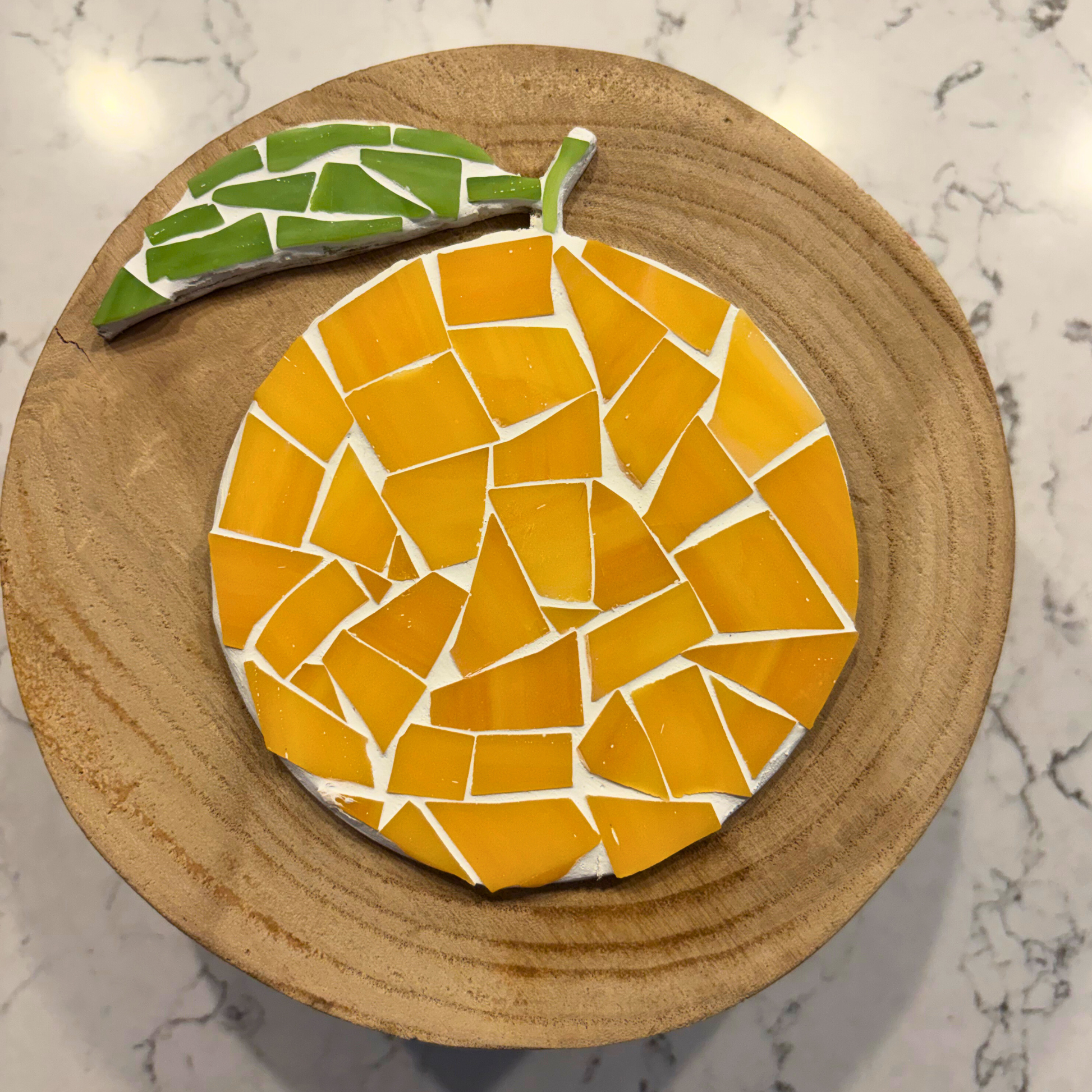 Mosaic orange coaster on a wooden base with a marble background